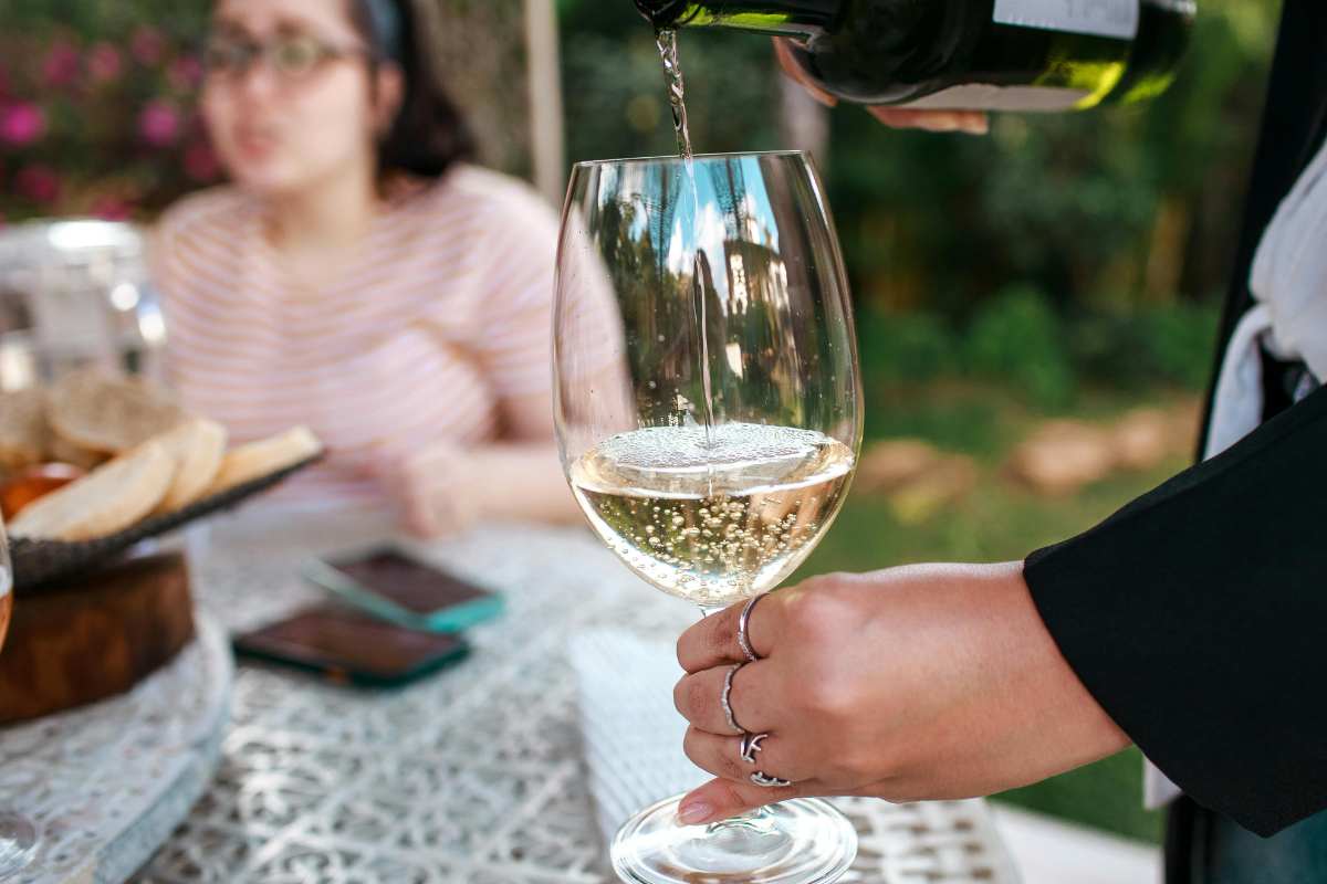 bicchiere di vino bianco in mano con persona che versa 